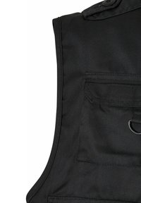 Mustasta kestävän kankaan tehdasliivi, jossa on rintatasku, rengasdetaili ja ryhdikkäät hartiat. Sileä pinta, näkyvillä saumoilla.