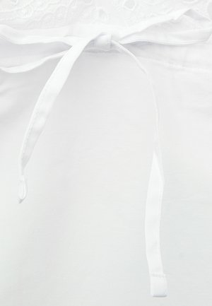 Zbliżenie białego pasa ubrania z niezawiązaną tkaninową kokardą na sznurku i fakturowanym górnym brzegiem.