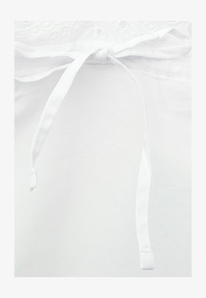 Zbliżenie białego pasa ubrania z niezawiązaną tkaninową kokardą na sznurku i fakturowanym górnym brzegiem.