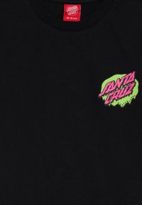 Črna bombažna majica s pisanem zelenim in roza logotipom "Santa Cruz Skateboards" na levi strani prsnega dela.
