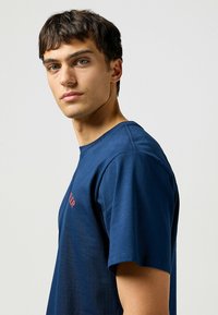 Laivastonsininen puuvillainen crew-neck t-paita lyhyillä hihoilla, jossa on punaista tekstiä rinnassa. Sujuva pinta ja rento malli.