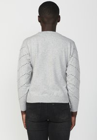 Maglione grigio con maniche lunghe, caratterizzato da un orlo a coste e cuciture diagonali testurizzate sulle maniche. Realizzato in un materiale morbido e leggero.
