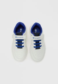 Baskets pour enfants de la marque Champion blanches et bleues avec des attaches Velcro et des lacets bleus sur un fond blanc.