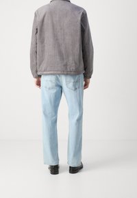 Grå fløjl jakke med krave, opkrøllede ærmer og rundet kant, parret med lyseblå lige ben jeans og sorte sko.