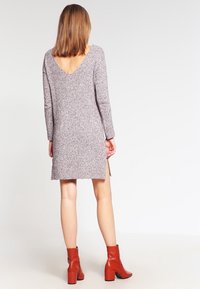 Ljusrosa stickad klänning med långa ärmar, djup V-rygg, sidofickor och bärs med röda ankelskor. Texturerad tyg lägger till detaljer.