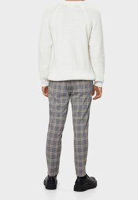 White knitted sweater with a textured finish, paired with gray plaid trousers featuring lines in black and beige, and black footwear.