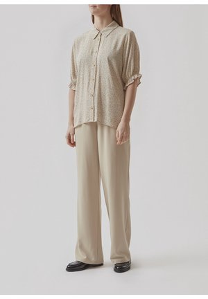 Svetle béžová blůza s květinovým vzorem, krátkými nadýchanými rukávy a zapínáním na knoflíky. V kombinaci s volnými krémovými kalhotami a černými botami.