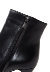 Botín negro de cuero hasta el tobillo con una textura suave, forma estrecha y cremallera lateral con etiqueta YKK, diseñado para un ajuste ceñido.