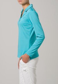 Turkos långärmad polo skjorta i mjukt, luftigt tyg; har en klassisk krage och en subtil logotyp på bröstet.