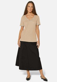 Beige T-shirt met korte mouwen en een V-hals met zwarte afwerking, gecombineerd met een lange zwarte rok. Textuurstof en een knie-lengte silhouet. Zwarte schoenen.