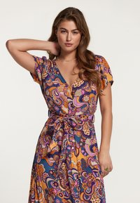 Barevné šaty s vzory, které obsahují paisley design v purpurové, oranžové a modré barvě. Krátké rukávy, výstřih do V a detail uvázaného pasu. Hladká tkanina.