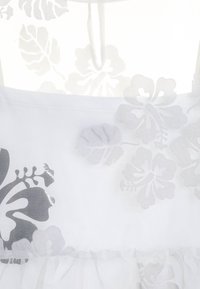 Bílé šaty s šedým květinovým vzorem, vyrobené z průsvitného materiálu a s vrstveným designem. Obsahují volánkový lem a hladkou texturu.