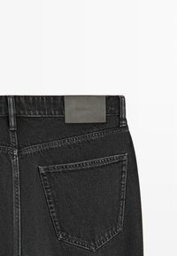 Bagfra udsigt af sorte cowboybukser med højre baglomme og en mørkegrå lædermærke med mærke på linningen.