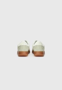 Baskets avec un upper en daim vert clair, des accents blancs, et une semelle extérieure en caoutchouc marron. Présente le logo de la marque sur le talon et un design de bout arrondi.