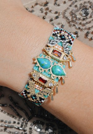Perlenarmband mit Türkis-, Rot- und klaren Steinen, goldenen Akzenten und einem gemusterten Band in Schwarz, Weiß und Teal.