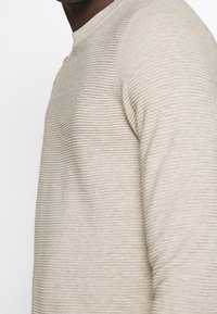 Pull en maille beige avec rayures horizontales, col rond et manches longues, fabriqué en matière douce et texturée.