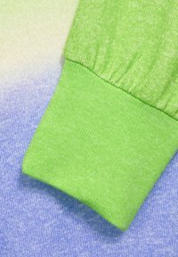 Grön ribbad mudd övergår till en gradient av ljusgrön till blå, tillverkad av mjukt stickat tyg med en texturerad yta.