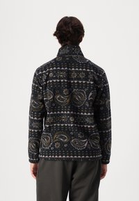 Herren Fleecejacke mit Muster in dunklen Tönen, versehen mit Paisley- und Blumenmustern, einem Kragen und langen Ärmeln. Weicher Stoff.
