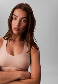 Lyserød trådløs bh med V-udskæring, brede stropper, glat tekstur og uden synligt hardware, hvilket giver et sømløst udseende.