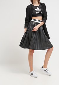 Gonna nera plissettata con una cintura bianca a righe, abbinata a un top cropped Adidas nero e a un blazer nero. Sneakers Adidas bianche.