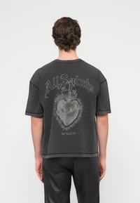 Μαύρο υπερμεγέθες T-shirt με χαμηλή ραφή στους ώμους, που διαθέτει γραφικό σχέδιο με καρδιά και στέμμα και κείμενο "All Saints" σε αντίθετο λευκό χρώμα.