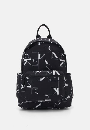 Zaino nero con motivi geometrici bianchi a lettere, dotato di una tasca frontale con zip e spallacci regolabili. Il materiale appare durevole e testurizzato.