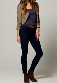 Brun mockaläderjacka i cropped-stil över en marinblå tanktop, kombinerad med mörka slim-fit jeans och bruna ankelstövlar med rosa sula.