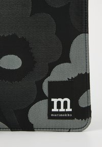 Black fabric bag with large gray floral print. Features a black label with white logo "marimekko" and textured stitching.