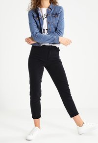 Chaqueta de mezclilla en azul claro con botones de metal, camiseta blanca con texto negro, pantalones ajustados negros y zapatillas blancas.