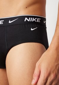 Svart Nike-kortbyxa med en vit logotyp på midjebandet och en vit swoosh på framsidan, med en slät yta och tät passform.