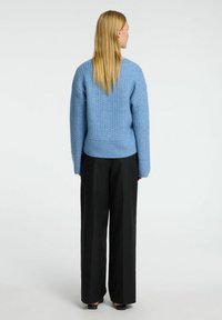 Lyseblå strikket sweater med et struktureret mønster, v-hals og en let cropped pasform, parret med sorte bredbenede bukser.