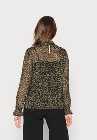 Blouse transparente avec un imprimé léopard en olive et noir, avec un col froncé, une fermeture à boutons au dos et des poignets de manches volants.