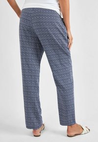 Pantaloni a righe navy con design a diamond; tessuto leggero, vestibilità rilassata e tasche laterali, abbinati a sandali bianchi.