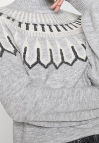 Suéter gris con un cuello alto. El cuerpo presenta un patrón geométrico en crema y negro, con un diseño de punto suave y texturizado.