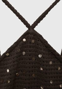 Tamno smeđa čipkana majica sa ukrštenim trakama i sjajnim okruglim sequins koji su ravnomjerno raspoređeni po površini radi dodatne detaljnosti i teksture.