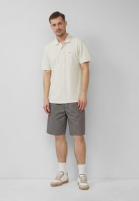 Helles beige Polo-Shirt, graue Shorts und weiße Socken kombiniert mit lässigen Sneakern. Angenehme Textur und einfaches Design. Keine sichtbaren Muster.