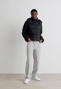 Giacca nera in pile con colletto alto, chiusura con zip e bottoni a scatto. Abbinata a jeans grigio chiaro e sneakers bianche. Design semplice.