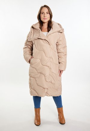 Cappotto imbottito beige con design trapuntato, colletto oversize e tasche laterali. Abbinato a jeans blu e stivaletti marroni.