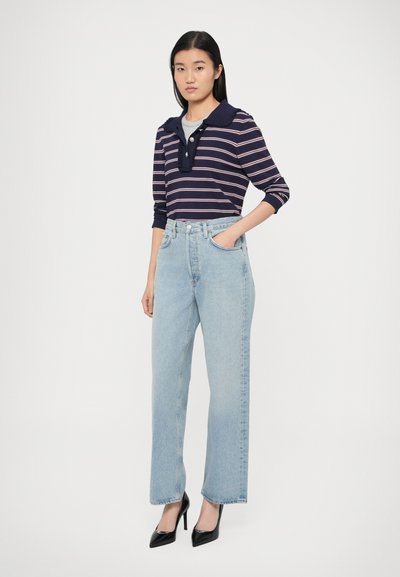 Granatowo-biała pasiasta długa koszulka polo z kołnierzykiem, w połączeniu z jasnoniebieskimi dżinsami z wysokim stanem i czarnymi szpilkami z zaostrzonym noskiem.