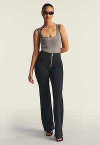 Camiseta de tirantes gris acanalada combinada con pantalones de campana negros de tiro alto, con una cremallera dorada y una textura suave y elegante. Unas gafas de sol negras complementan el conjunto.