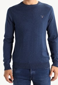 Pull bleu marine à col rond en tissu doux, avec poignets et ourlet côtelés, et un petit logo sur la poitrine.