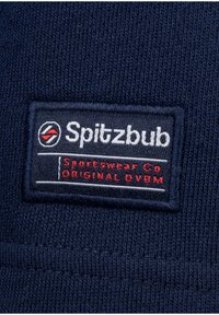 Navy blue fabric patch featuring "Spitzbub Sportswear Co" in white and red text, with a logo design above. Textured knit background.