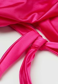 Tela de satén fucsia con una textura suave, que presenta un detalle de cinta atada. El material muestra brillo y un color sólido sin patrones.