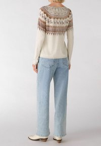 Pull crème à manches longues avec des motifs géométriques marron sur les épaules, assorti à un jean large bleu clair et des bottines crèmes.
