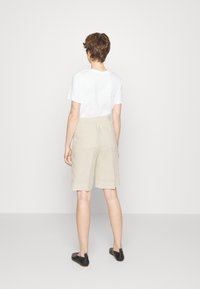 Béžové lněné kraťasy s uvolněným střihem, bočními kapsami a středním pasem, sladěné s bílým bavlněným tričkem a černými nazouvacími botami.