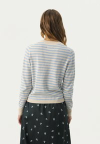 Stribet sweater i lyseblå og beige, strikket materiale, rund halsudskæring, ribbede manchetter, parret med en sort nederdel med blomsterprint.