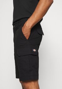 Shorts cargo noirs en tissu durable, dotés de poches latérales, d'une fermeture à bouton et d'un patch logo de la marque sur la jambe gauche.