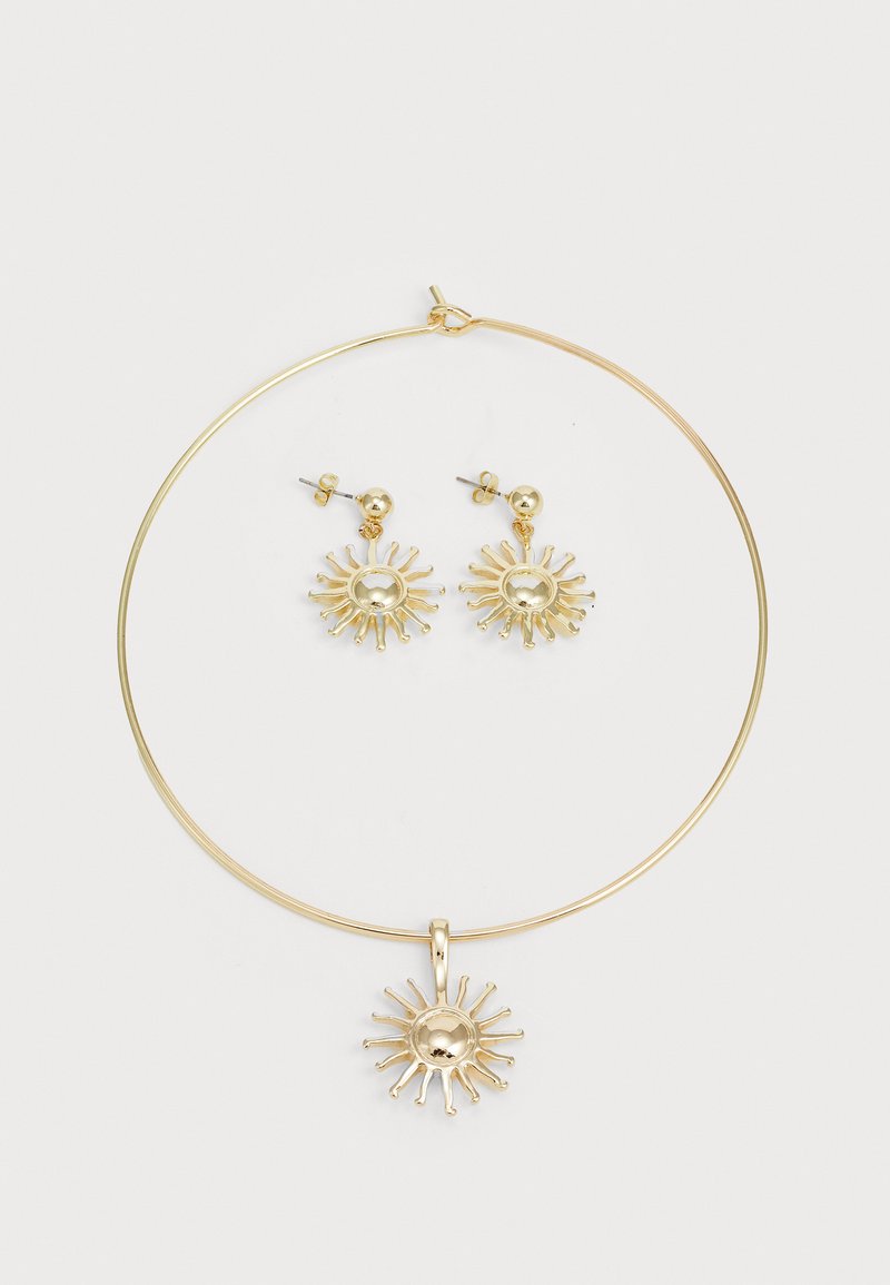 Gull jewelry-set med en sirkulær halskjede med en solpendant og matchende solformede stiftøreringer, alle med en polert finish.