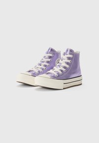 Fialové vysoké plátenné tenisky s bielymi šnúrkami, bielou gumovou špičkou a hnedou gumovou podrážkou s čiernymi prúžkami. Logo Converse na boku.