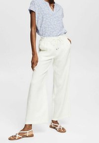 Blusa floreale azzurro chiaro con scollatura a V, abbinata a pantaloni bianchi a gamba larga con vita elastica e cordino. Sandali bianchi con fasce.